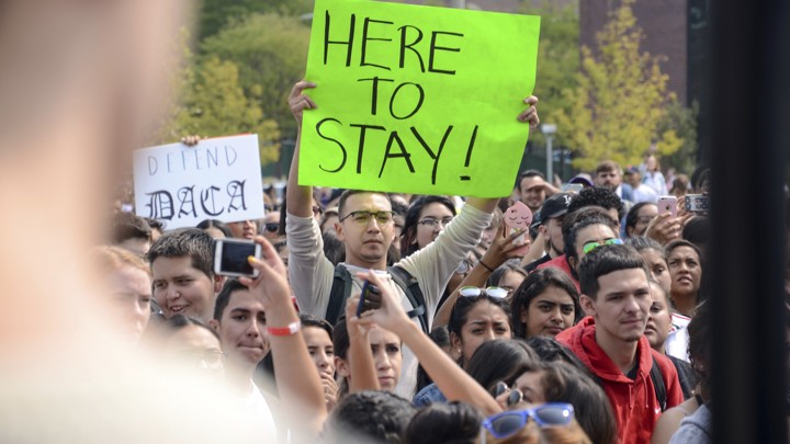 A protester holds a sign that reads "Here to Stay!"