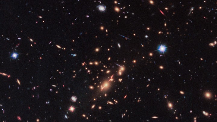 A Hubble Telescope image that includes a red, disk-shaped galaxy seen through a gravitational lens in the upper right corner.