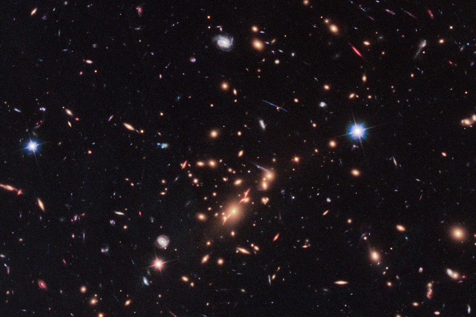A Hubble Telescope image that includes a red, disk-shaped galaxy seen through a gravitational lens in the upper right corner.
