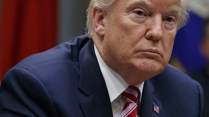 A close-up photo of President Trump in a meeting, wearing a navy suit and a red-and-blue tie