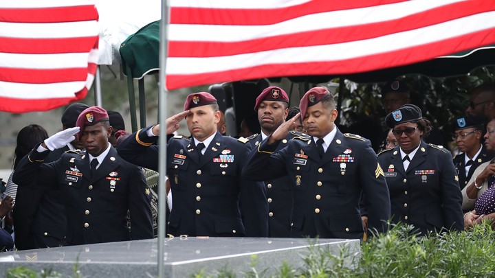 U.S. soldiers salute the casket of U.S. Army Sergeant La David Johnson with U.S. flags flying in the background.