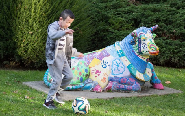 A little boy playing soccer next to a colorful statue of a cow