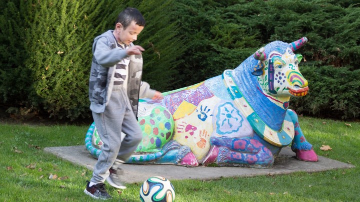 A little boy playing soccer next to a colorful statue of a cow