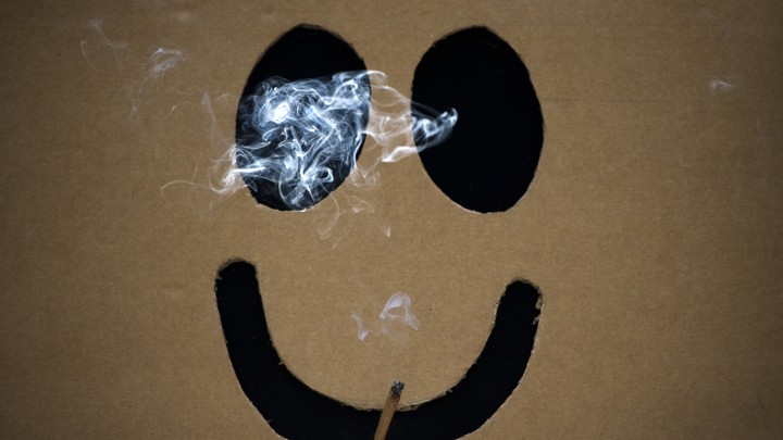 A smiley face smokes a joint of marijuana.