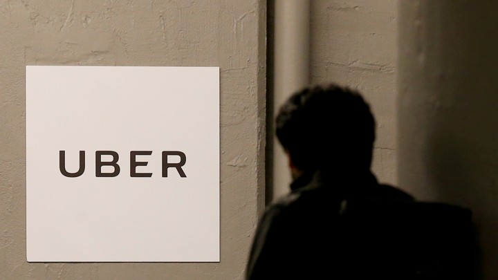A person walking past a wall with an Uber sign on it