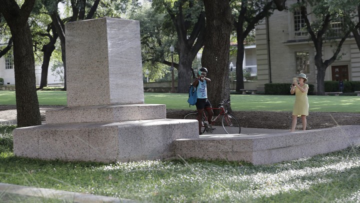 Two passersby take photos of a pedestal where a statue once stood.