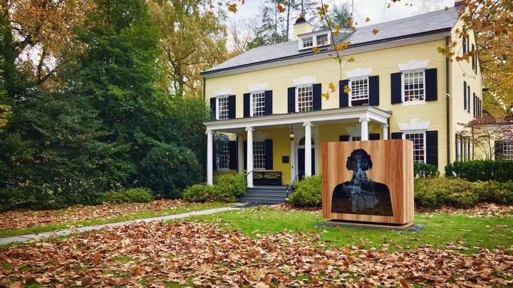 A sculpture of a bust with several image layers stands in front of a campus building at Princeton.