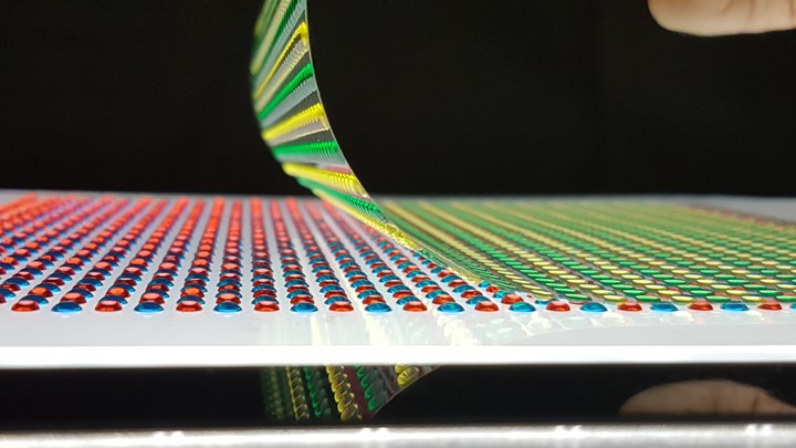A sheet of yellow and green dots is pulled off of or applied onto a sheet of red and blue dots.