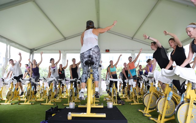 People ride yellow stationary bikes in an outdoor SoulCycle class.
