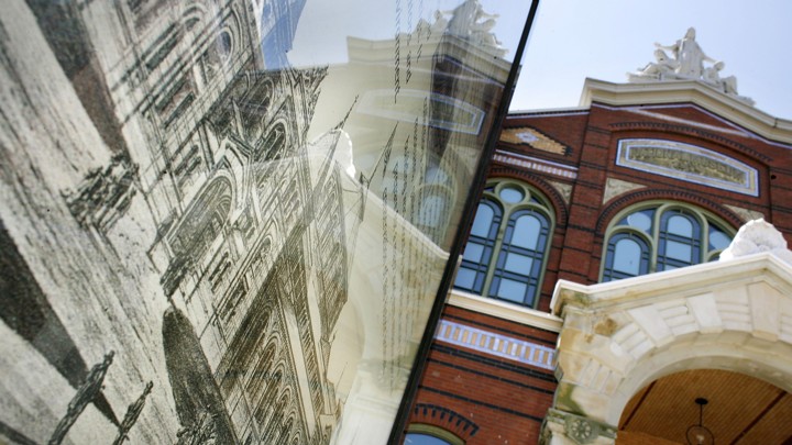 The Smithsonian Institution Arts and Industries Building is reflected in a sign displaying an antique drawing of the building
