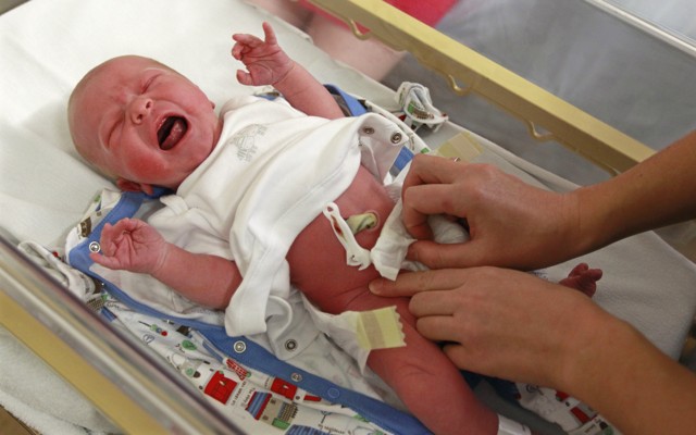 A crying baby is examined in a hospital crib.