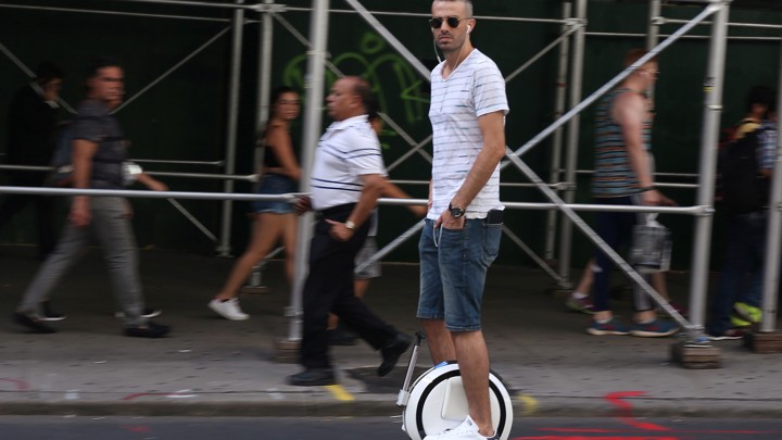 A person rides a one-wheeled hoverboard down a street.