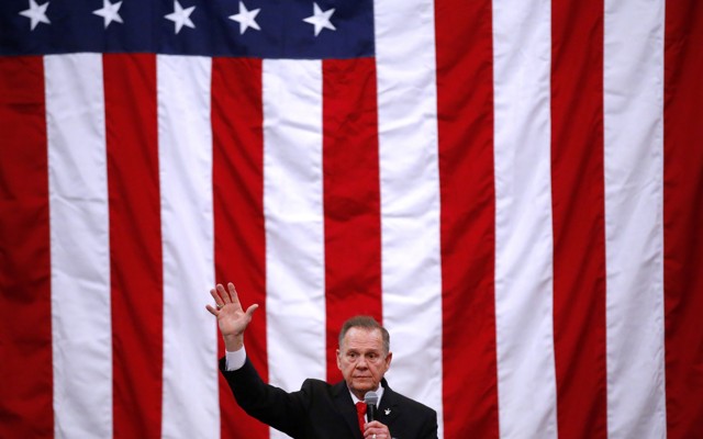 Roy Moore at a campaign rally with a giant American flag behind him