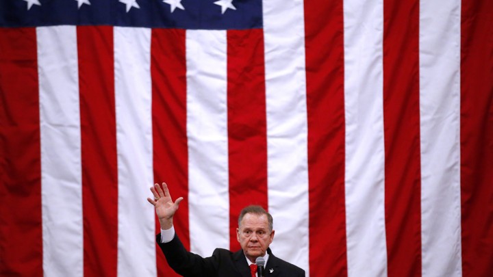 Roy Moore at a campaign rally with a giant American flag behind him