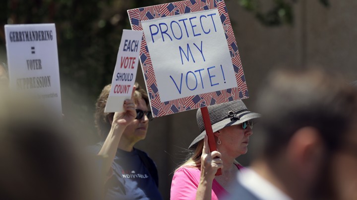 Protesters hold up signs reading "Gerrymandering = voter suppression," "Each vote should count," and "Protect my vote!"