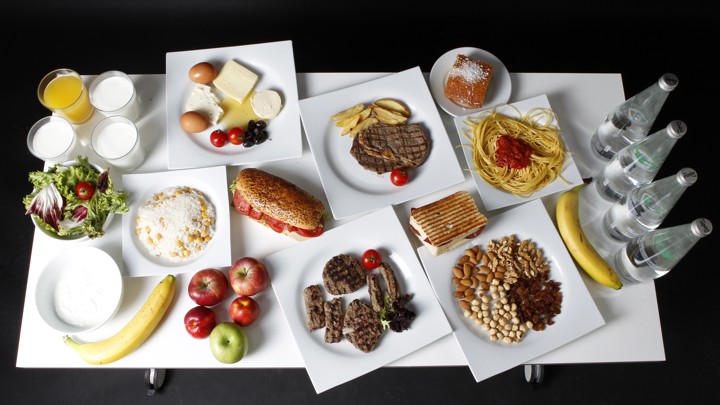 A table containing salad, fruit, water, pasta, meats, sandwiches, cheese, eggs, juice, and milk