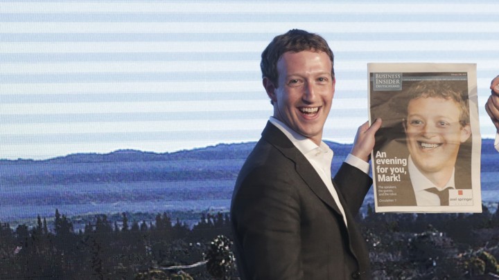 Facebook's Mark Zuckerberg holds a newspaper with a picture of him on it.
