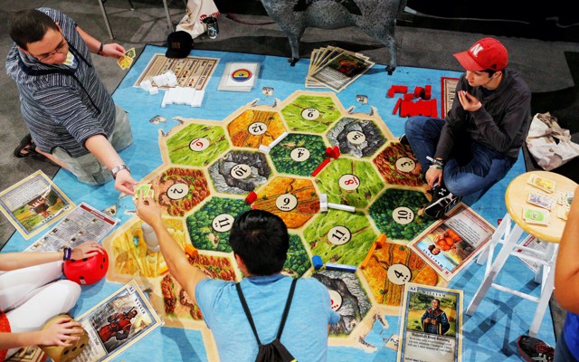 Three young men play the German board game Settlers of Catan