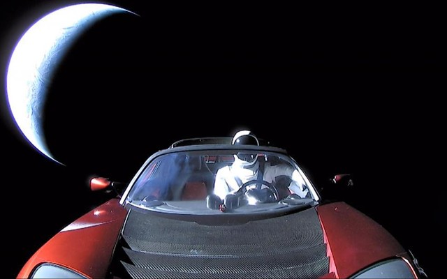 The dummy astronaut Starman, wearing a SpaceX space suit, in the driver's seat of a red Tesla Roadster in space as it speeds away from Earth