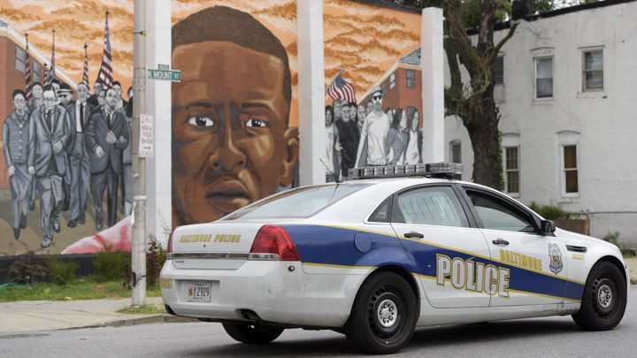A Baltimore Police car passes a mural of Freddie Gray.