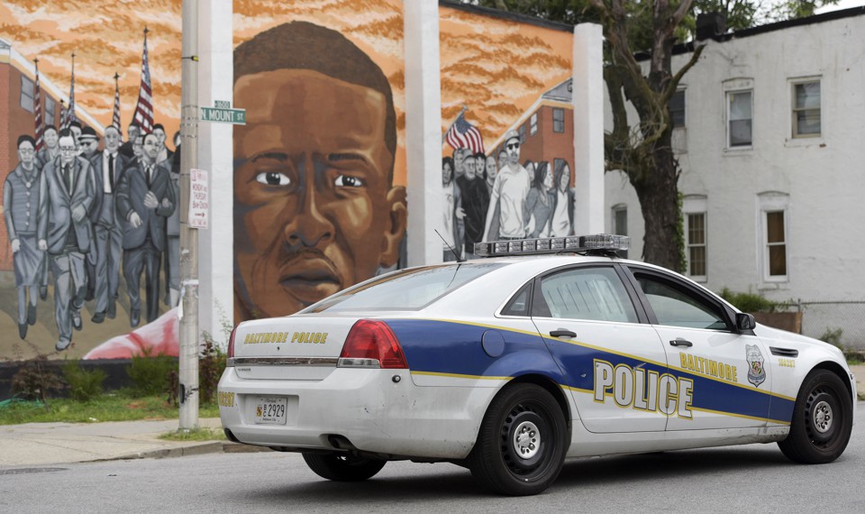 A Baltimore Police car passes a mural of Freddie Gray.