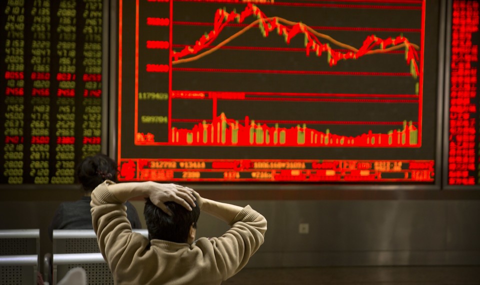 An investor holds his head in front of a red screen with fluctuating stock prices