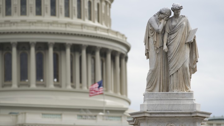 An American flag flies at half staff over the U.S. Capitol and behind the Peace Monument in Washington, D.C.