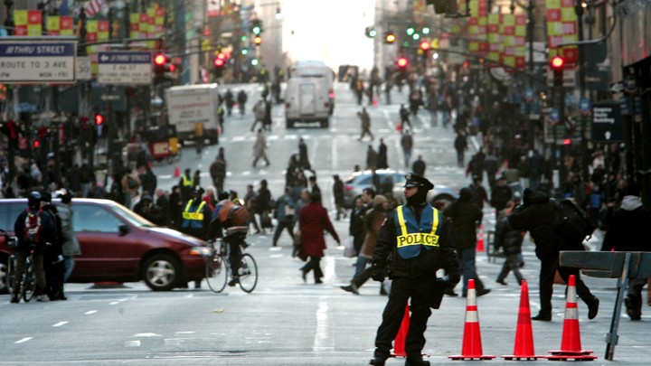 A police officer blocks traffic as pedestrians, bikers, cars, and trucks negotiate Fifth Avenue in New York.