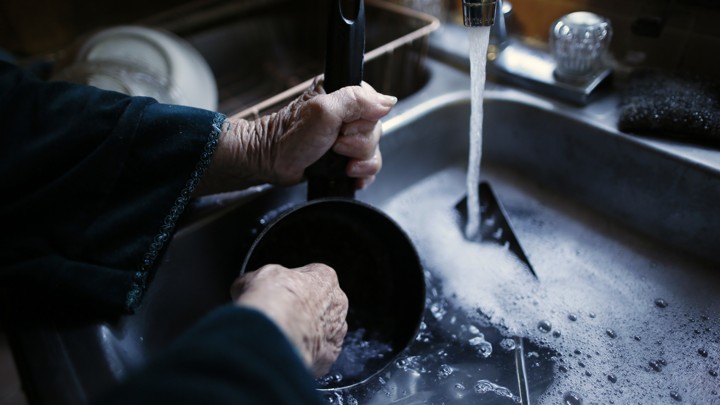 An elderly woman's hands washing a pot in a sink