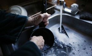 An elderly woman's hands washing a pot in a sink