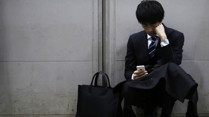 A man leaning against a wall looks down passively at his iPhone