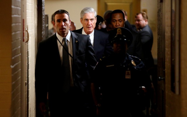 Special Counsel Robert Mueller and other officials walk down a hallway accompanied by a police officer.