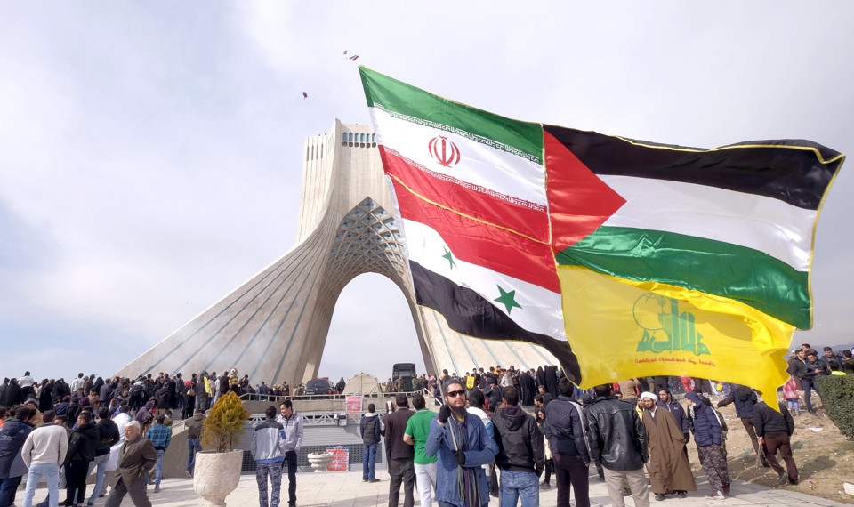 A man carries a giant flag made of flags of Iran, Palestine, Syria and Hezbollah in Tehran.