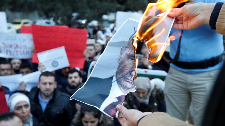Protesters burn a picture of Vladimir Putin.