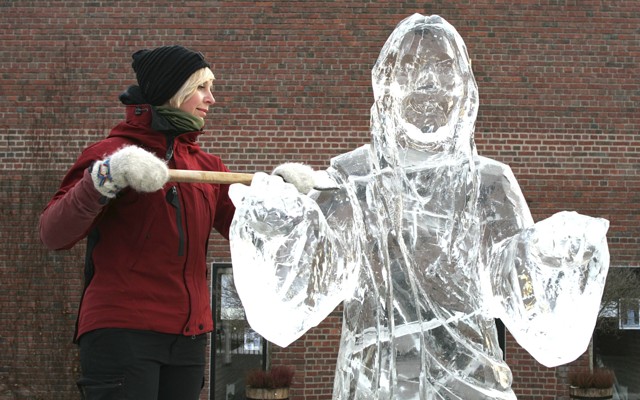 A woman raises an ice-scraping tool next to an ice sculpture of Jesus Christ.