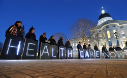 En tenant des pancartes, les membres d'un groupe pro-Medicaid organisent un rassemblement devant un bâtiment gouvernemental dans le Maine.