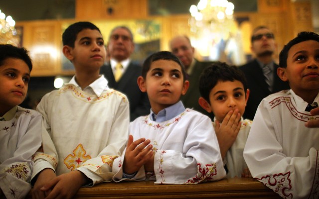 Five boys lean on a wooden pew at a Coptic Orthodox church.