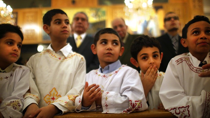 Five boys lean on a wooden pew at a Coptic Orthodox church.
