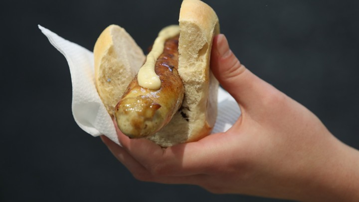 A hand holding a rostbratwurst pork sausage with mustard on top of it