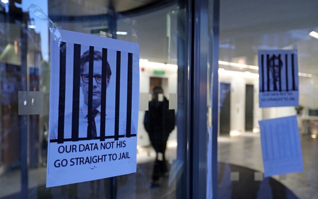 Posters hang on a glass door depicting the Alexander Nix behind bars with the text, "Our Data Not His. Go Straight to Jail."