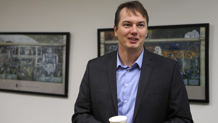 Chris Urmson standing in front of two framed pictures and holding a cup