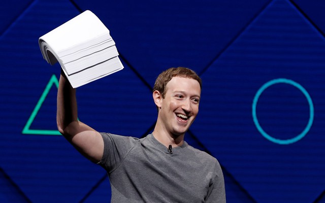Mark Zuckerberg holds a stack of papers aloft, against a blue background. 