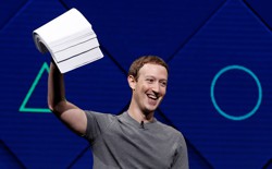 Mark Zuckerberg holds a stack of papers aloft, against a blue background. 
