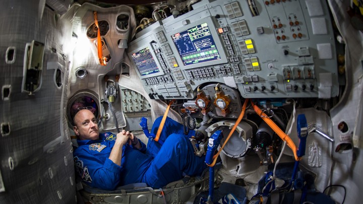 Scott Kelly in a blue NASA space suit at a control panel on the International Space Station