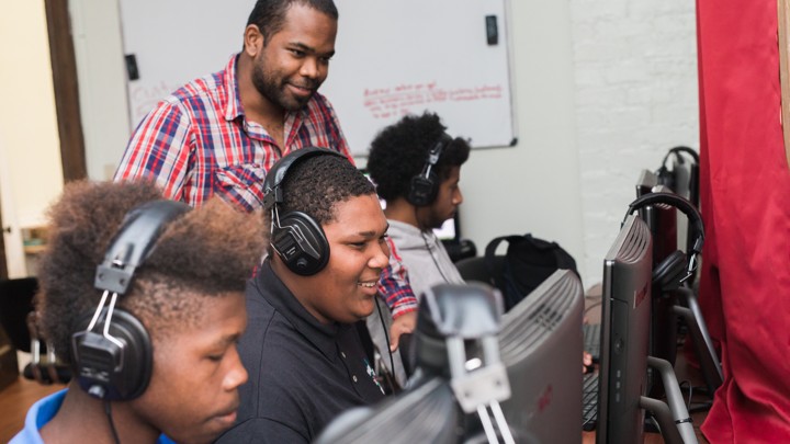 Young men wearing headphones work on graphic design on their computers.