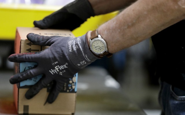 A person wearing a watch and gloves handles an Amazon package.