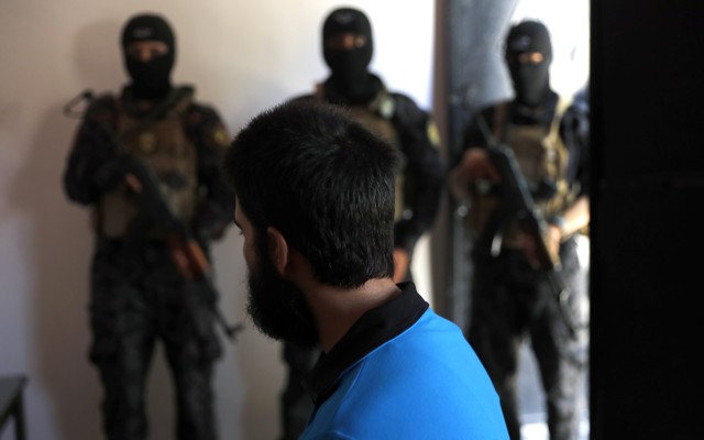 Kurdish soldiers from the Anti-Terrorism Units stand in front a suspected Islamic State member 