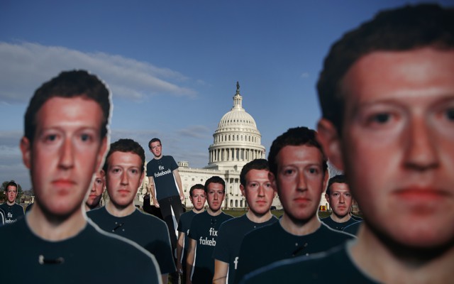 Cardboard cutouts of Mark Zuckerberg's face dominate the foreground, while the dome of the U.S. Capitol looms in the background.