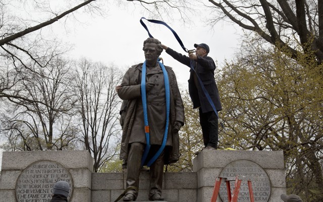 A worker tosses a strap over a statue