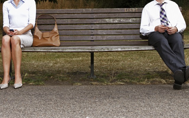 A woman and man sitting far apart on a bench